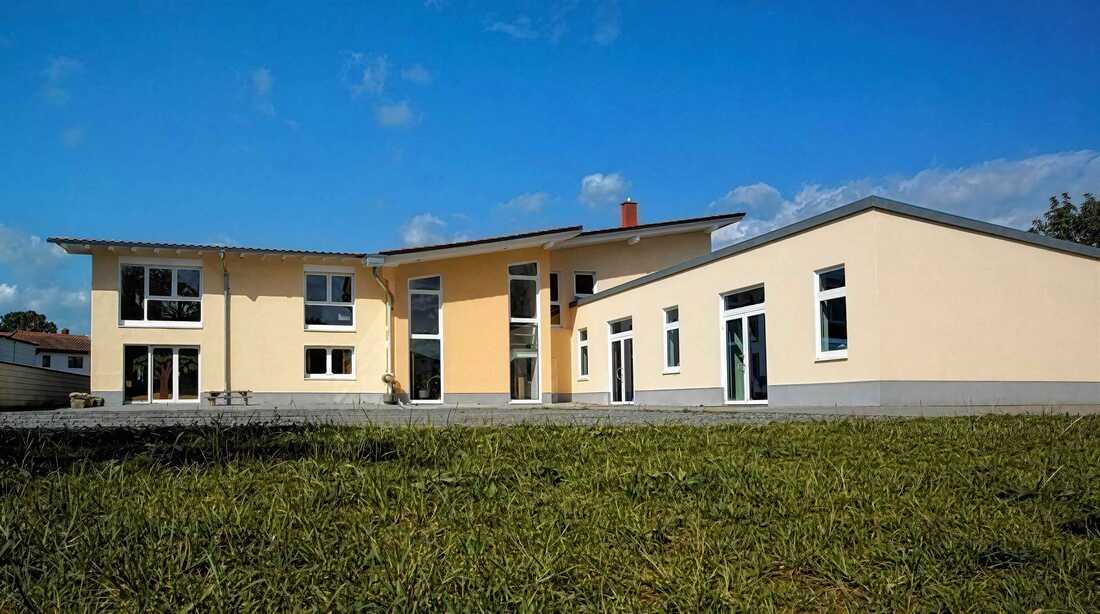 Außenansicht der Senfkornschule in Bensheim – ein modernes, cremefarbenes Schulgebäude mit großen Fensterfronten unter blauem Himmel.